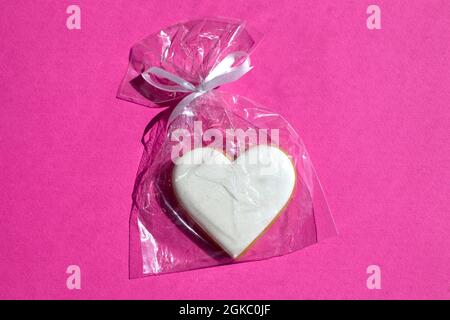 Gingerbread heart decorated with icing in gift plastic bag with ribbon on bright pink background flat lay Stock Photo