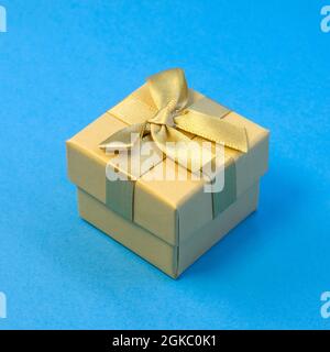 Closed golden gift box with silk gold ribbon bow on bright blue background close up Stock Photo