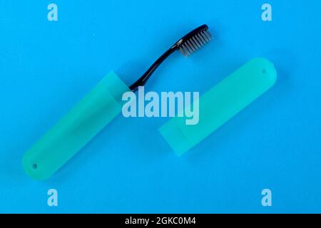 Close-up side profile macro view photo of packed in plastic trip case cover with cap black toothbrush on bright blue background Stock Photo