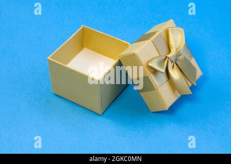 Empty golden gift box with silk gold ribbon bow on bright blue background close up Stock Photo