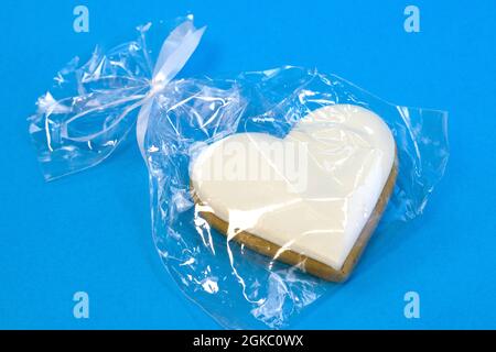 Gingerbread heart decorated with icing in gift plastic bag with ribbon on bright blue background flat lay Stock Photo