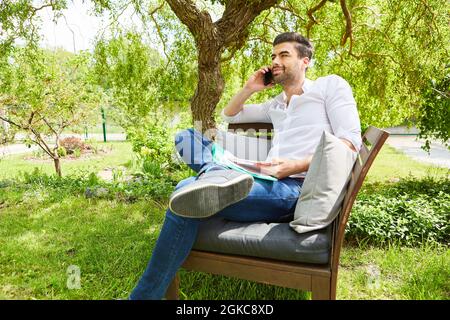 Freelancer man talking on the mobile phone in the green garden in summer Stock Photo