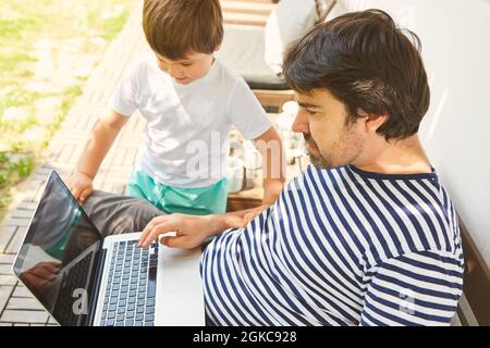Freelancer as a father on the laptop computer together with his son at home Stock Photo