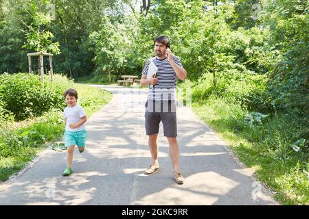 Single father talking on mobile phone with son in green park on vacation Stock Photo