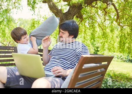 Child annoys and disturbs single father while working on the computer in the garden Stock Photo