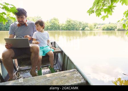 Father and son using laptop computer in a boat at the lake in summer as freelancers Stock Photo