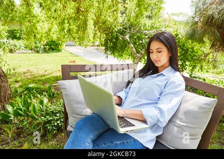 Young woman on laptop PC in green garden as home office in summer in nature Stock Photo