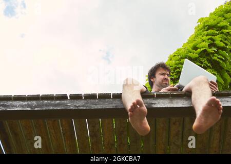 Programmer works on the way in summer with his laptop computer on a jetty by the lake Stock Photo