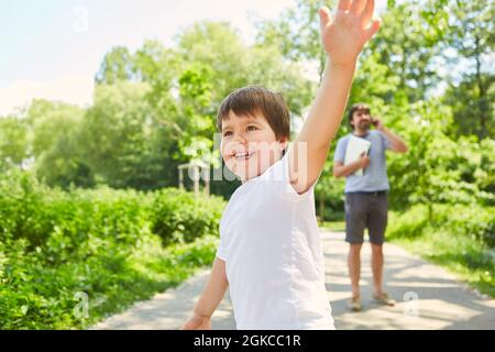 Father talking on mobile phone in park in summer with son playing in foreground Stock Photo