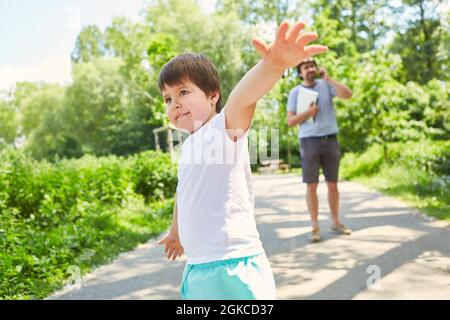 Child playing in the park on summer vacation with father making mobile phone call in the background Stock Photo