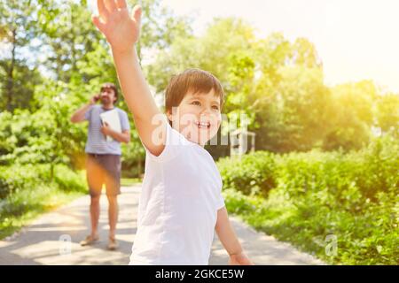 Happy child playing in nature in summer while father is talking on the phone in the background Stock Photo