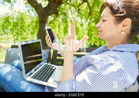 Freelancer woman using smartphone and laptop computer while watching video Stock Photo