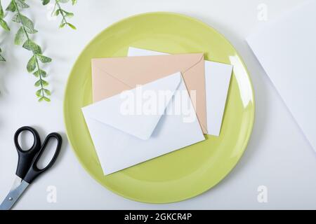 Composition of envelopes on green plate, scissors and branches on white background Stock Photo