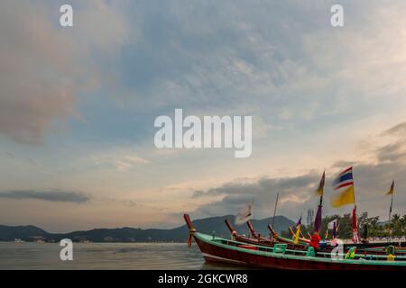 long tail boats moored on the shore of a Thai beach with their flags flapping in the wind at dawn of a new day Stock Photo