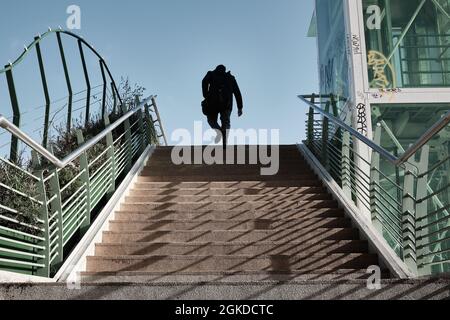 A man going to work on a sunny morning. He's walking up the final stairs of a bridge. Only his silhouette is recognizable. Stock Photo