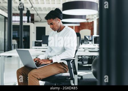 Male programmer working on a new project in an office. Focused young businessman using a laptop while sitting alone in a modern workplace. Young softw Stock Photo