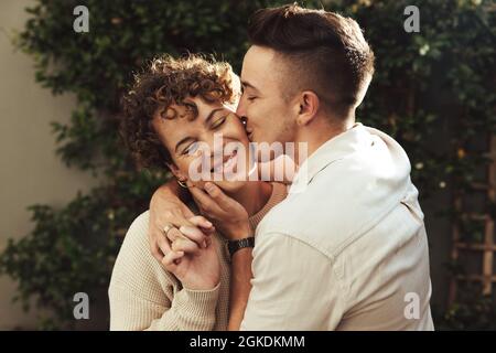 Affectionate young man kissing his girlfriend outdoors. Romantic young man kissing his girlfriend on the cheek while embracing her. Young LGBTQ+ coupl Stock Photo