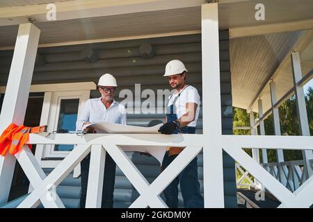 Pair of construction engineers reading drawings on porch Stock Photo