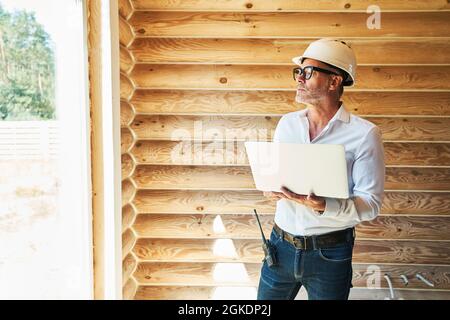 Distracted engineer with laptop staring outside from house Stock Photo