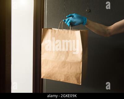 Hand holding paper bag with food in doors, in medical gloves, copy space. Safe grocery delivery, courier during coronavirus quarantine. Stock Photo