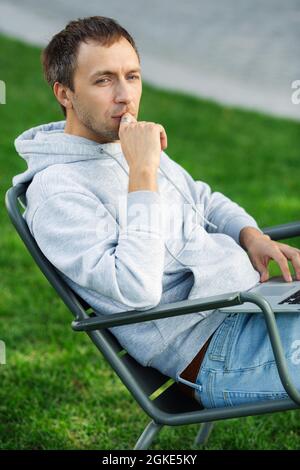 Business entrepreneur work on laptop outdoors sitting on chair in backyard or park emailing remotely Stock Photo