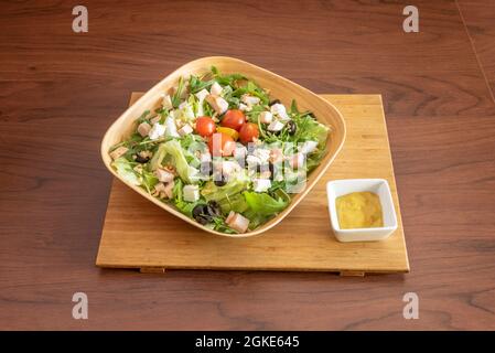 wonderful salad served in a bamboo wood bowl with jam tacos, red and yellow cherry tomatoes, chopped fresh cheese, slices of black olives and dried fr Stock Photo