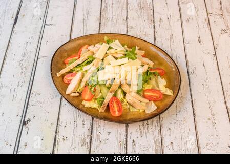 arugula and iceberg lettuce salad with grilled chicken fillet strips, split cherry tomatoes and sliced cheese on white wooden table Stock Photo