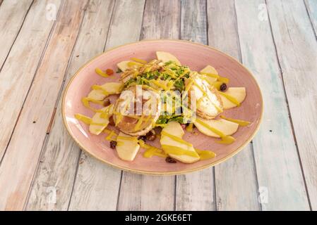 Gourmet salad of goat cheese, orange slices, lettuce and nuts on a pink plate and wooden table. Stock Photo