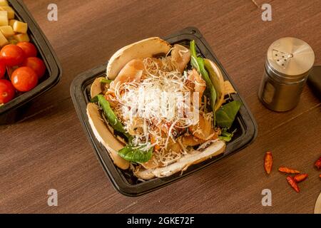 Spinach salad with grated cheese, slices of raw mushrooms, sliced bacon and cayenne in a takeaway container Stock Photo