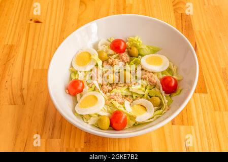 White bowl of mixed canned tuna salad with boiled egg, cherry tomatoes, iceberg lettuce and Spanish pitted olives Stock Photo