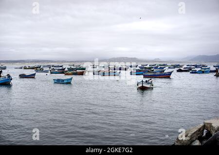 El Dorado, Peru - July 30, 2021: Men operating small fishing boats with small moored fishing boats, beach and mountains in background Stock Photo