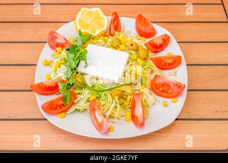 Turkish salad with fresh square cheese, sweet corn, iceberg lettuce with lots of tomato wedges, pitted Spanish olives and a sprig of parsley. Stock Photo