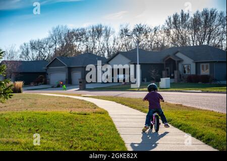 Caucasian 3 yr old boy ridding a pink balance bike on a sidewalk in a residential neighborhood  Stock Photo