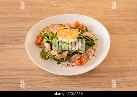 Fried spinach and goat cheese salad with fried bacon, pine nuts and cherry tomatoes with balsamic vinegar Stock Photo