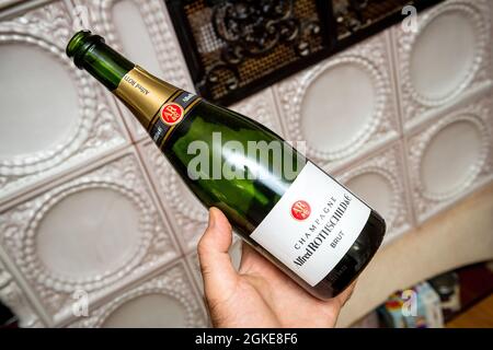 Man holding new empty bottle of Alfred Rothschild and Company champagne bottle with luxury oven in background