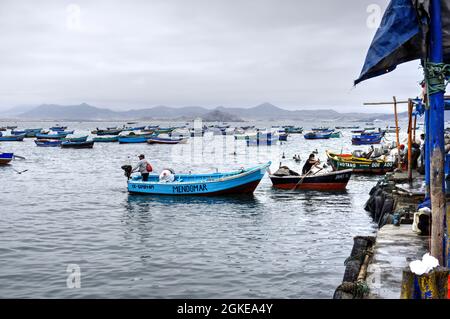 El Dorado, Peru - July 30, 2021: Men operating small fishing boats with small moored fishing boats, beach and mountains in background Stock Photo