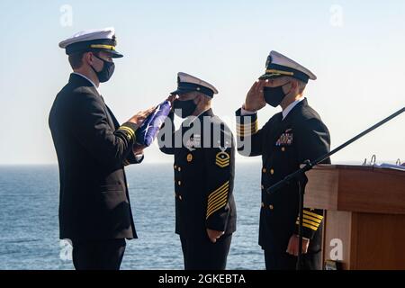 PACIFIC OCEAN (March 29, 2021) Capt. Aaron Taylor, executive officer aboard Wasp-class amphibious assault ship USS Essex (LHD 2), right, and Command Master Chief Augustine Cooper, middle, salute the national ensign during a burial at sea ceremony. Essex is underway conducting routine operations in U.S. Third Fleet. Stock Photo