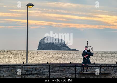 Piper plays bagpipes at dawn commemorating St Valery Day when Scottish soldiers were captured in WW II with Bass Rock, Scotland, UK Stock Photo