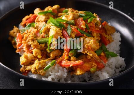 Thai breakfast Gai Pad Pongali with chicken, eggs, spicy, yellow thai curry paste,tomato, rice in black bowl made in wok. Close up. Pan-Asian cuisine. Stock Photo