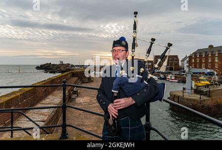 Piper plays bagpipes at dawn commemorating St Valery Day (Scottish soldiers captured in WW II) North Berwick harbour, East Lothian, Scotland, UK Stock Photo