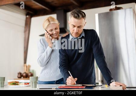Couple wife and husband having breakfast in the morning before work, taking notes, talking on mobile phone Stock Photo