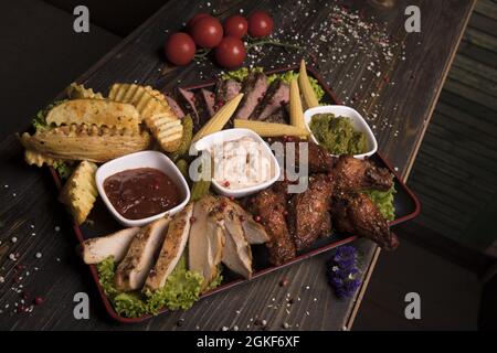 Meat assortment of fried chicken wings, beef, and pork decorated with lettuce, cherry tomatoes Stock Photo