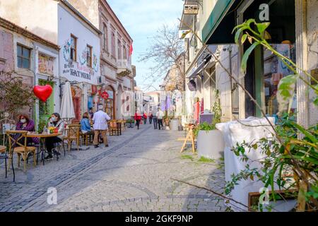 Urla, Izmir, Turkey - 03.08.2021: beautiful local traditional street in a clear air and vendors and people with mask sitting Stock Photo