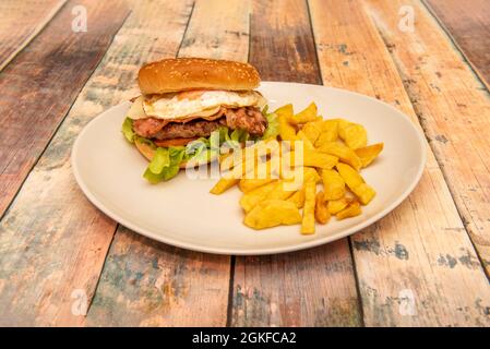 Classic beef burger with fried egg and delicious yolk with double melted cheese and fried bacon with tomato and lettuce and a garnish of homemade chip Stock Photo