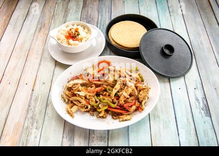 set of ingredients to prepare chicken fajitas with sautéed peppers, white rice with pico de gallo and corn tortillas on wooden table Stock Photo