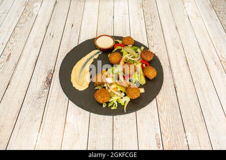 Falafel balls with lettuce salad and pickled gherkins with a little chickpea hummus on a black slate plate Stock Photo