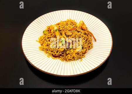 Chinese curly rice noodles with sautéed vegetables and pork and prawns with yakisoba sauce on white plate and brown stripes Stock Photo
