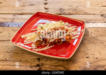Mexican style chicken flutes on pretty red plate and vintage wood table Stock Photo