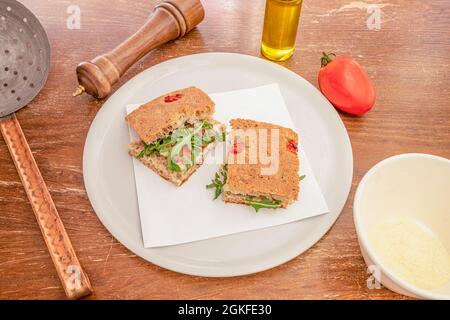 traditional Italian focaccia recipe with arugula, cheese and dried tomato on a white plate and with a pepper shaker, grated Parmesan cheese and olive Stock Photo