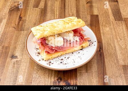 Italian focaccia with Iberian ham and cheese, black pepper and olive oil on wooden table Stock Photo